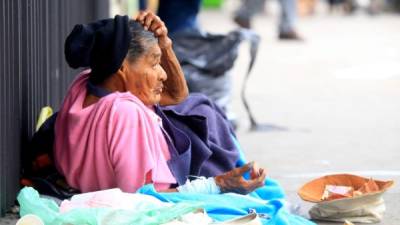 Acostada en el suelo y abrigada con una cobija vieja, esta señora utiliza su sombrero como recolector de dinero.