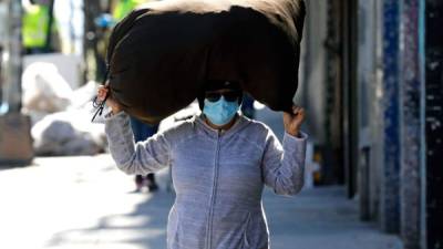 Una mujer usa una máscara facial protectora mientras lleva un saco en la cabeza en El Bronx. Foto EFE