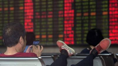 Un inversionista revisa su teléfono frente al tablero que anuncia los resultados de la Bolsa en Shangjai, China.