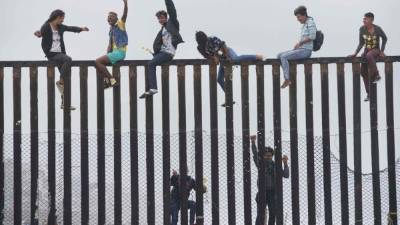 Manifestantes de la caravana suben la valla fronteriza entre Estados Unidos y México durante un mitin. AFP