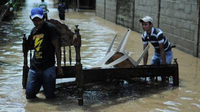 Fotografía de archivo en la que se registró a dos hombres al cargar una cama en medio de una calle inundada por un fuerte temporal, en el municipo de Marcovia, en el sur de Honduras.