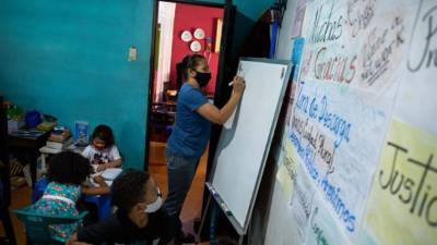 La maestra Jasmín Castro escribe en una pizarra durante una clase en su casa