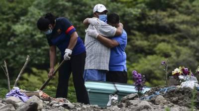 Men mourn during the burial of a COVID-19 victim at an annex of the Parque Memorial Jardin de Los Angeles cemetery, acquired by the municipality to bury people who died from the new coronavirus, 14 km north of Tegucigalpa on June 17, 2020. - Honduras has so far registered 9,658 contagions and 478 deaths from COVID-19. (Photo by ORLANDO SIERRA / AFP)