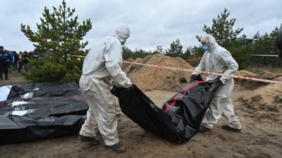 Los forenses llevan el cuerpo de uno muertos enterrados en una fosa común en un cementerio cerca de Lyman, región de Donetsk.