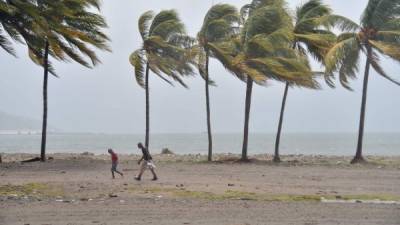Haitian people walk through the wind and rain on a beach, in Cap-Haitien on September 7, 2017, as Hurricane Irma approaches. Irma was packing maximum sustained winds of up to 185 mph (295 kph) as it followed a projected path that would see it hit the northern edges of the Dominican Republic and Haiti on Thursday, continuing past eastern Cuba before veering north for Florida. / AFP PHOTO / HECTOR RETAMAL