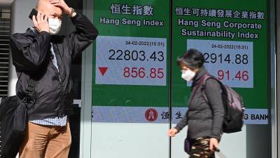 Un hombre usa su teléfono junto a un letrero que muestra los números del índice Hang Seng antes del cierre, cuando las acciones de Hong Kong cayeron el 24 de febrero de 2022 cuando se conoció la noticia de que Rusia invadió Ucrania.