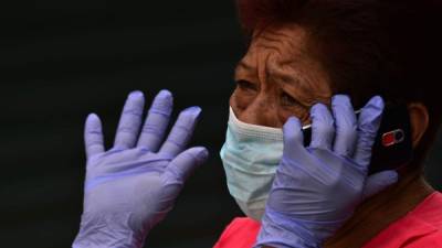 Una mujer usa una máscara facial y guantes contra la propagación del nuevo coronavirus mientras habla por su teléfono celular en un mercado en Tegucigalpa. AFP