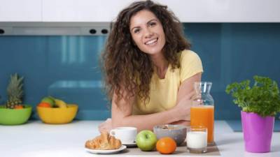 Young woman having breakfast at home, eating healthy food, fruits, milk, cereals and orange juice.