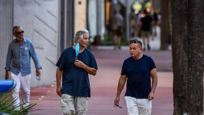 Dos hombres caminan sosteniendo máscarillas faciales en un centro comercial en Miami Beach. AFP