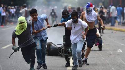 TOPSHOT - Anti-government activists drag a police motorbike burnt after the explosion of an explosive device during a protest against the elections for a Constituent Assembly in Caracas on July 30, 2017.Deadly violence erupted around the controversial vote, with a candidate to the all-powerful body being elected shot dead and troops firing weapons to clear protesters in Caracas and elsewhere. / AFP PHOTO / Ronaldo SCHEMIDT