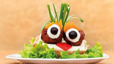 Albóndigas sobre sándwich de queso con ensalada. Coloque aceitunas negras para los ojos y queso cheddar para las cejas.