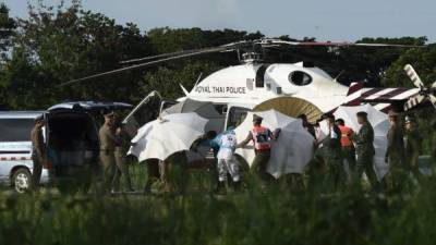 Personal policial y militar usa sombrillas para cubrir una camilla cerca de un helicóptero y una ambulancia en un aeropuerto militar en Chiang Rai.