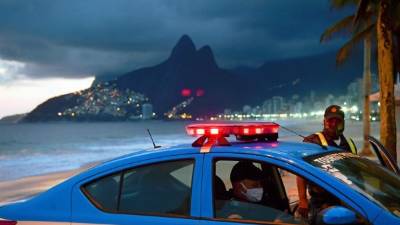 La policía con máscaras faciales como medida contra la propagación del nuevo coronavirus se ve con su automóvil en la playa de Ipanema en Río de Janeiro, Brasil, el 19 de mayo de 2020. / AFP / CARL DE SOUZA.