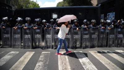 Una mujer camina frente a un contingente policial, desplegado para resguardar las sesiones de renegociación, las cuales han suscitado algunas protestas.