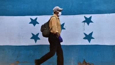 A man wearing a face mask against the spread of the new coronavirus walks past a wall depicting the Honduran flag in Tegucigalpa on April 2, 2020. - The number of the people infected with COVID-19 reached 219 Thursday in the Central American country. (Photo by ORLANDO SIERRA / AFP)
