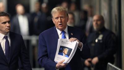 Trump muestra recortes de prensa a la salida de una audiencia en un tribunal de Nueva York.