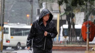 Hondureño se protege de la lluvia en Tegucigalpa utilizando una ‘chumpa’ mientras camina por una calle.