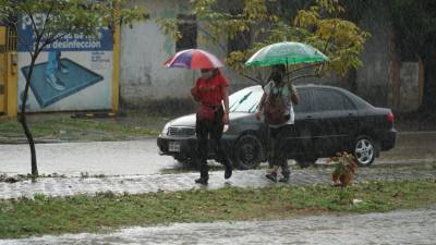 Dos personan caminan bajo una fuerte lluvia a orillas de una calle en San Pedro Sula (Honduras).