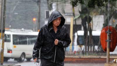 Hondureño se protege de la lluvia en Tegucigalpa utilizando una ‘chumpa’ mientras camina por una calle.