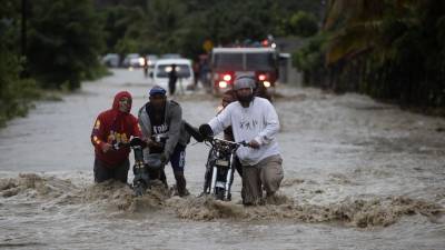 Personas cruzan con dificultad la carretera que se encuentra inundada producto de las intensas lluvias en San José de Ocoa (República Dominicana).