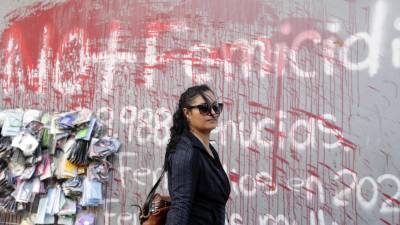 Una mujer camina frente a un muro pintado con un grafiti en contra de los feminicidios en Tegucigalpa.