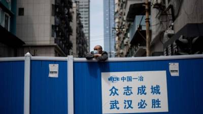 Un hombre con mascarilla se asoma sobre una barricada en un barrio de Wuhan, China, donde los científicos buscarán el origen de la pandemia.