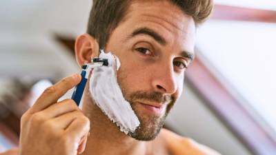 Shot of a handsome young man shaving at home