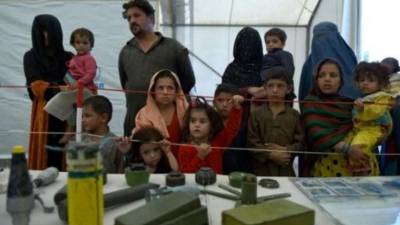 Unas familias de refugiados afganas miran modelos de bombas y minas mostrados en un campamento a las afueras de Kabul, hace tres años, un 27 de septiembre. Foto Archivo AFP.