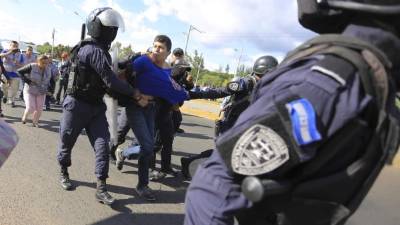 Policías detienen a supuestos estudiantes para efecto de investigación, cuando se manifestaban en el sitio donde buses de transporte urbano fueron quemados frente a la estatal Universidad Nacional Autónoma de Honduras (UNAH) el 6 de diciembre de 2018. EFE