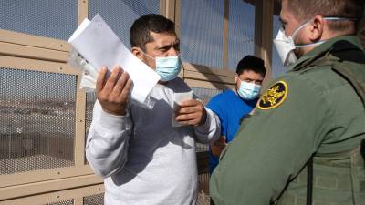 Dos migrantes centroamericanos hablan con un policía mientras son deportados bajo el programa reactivado “Quédate en México”.