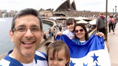 Claudio Díaz, Gabriela Luque, Alejandra y la pequeña Lily posan orgullosos con la bandera y camisas de Honduras en las cercanías de la ópera de Sídney.