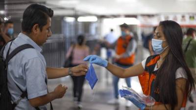 Una mujer entrega una mascarilla a un hombre para que se protega del contagio de coronavirus. Foto: AFP