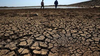 Fotografía tomada el 3 de abril de 2017, que muestra a dos obreros que caminan sobre la tierra agrietada del fondo de la presa 'Sábanas Blancas', que se encuentra por debajo del mínimo de su capacidad de embalse en la provincia de Ciego de Ávila (Cuba). EFE
