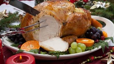 Carving roasted herb rubbed turkey garnished with fresh grapes, oranges, and cranberry is ready for Christmas dinner. Ornaments, Champagne, candles, and other Christmas decorations on feast table.