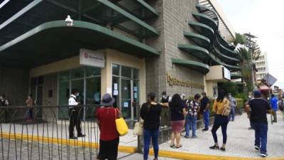 Varias personas hacen fila afuera de una agencia bancaria de San Pedro Sula.
