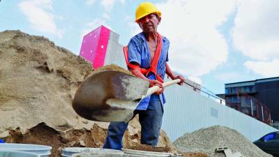 Un trabajador carga cubetas con tierra en una construcción, mientras en una plaza comercial en construcción solicitan albañiles y ayudantes. Fotos: M. Cubas./ M. Valenzuela