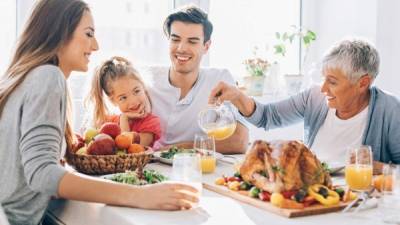 Happy multi-generation family sitting at the dining table with roasted turkey, salad and drinks