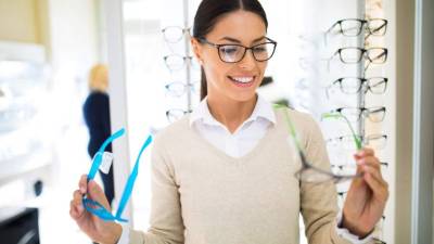 Young woman choosing glasses in optical shop. Front view.