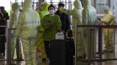 Personal médico con trajes protectores revisan a los viajeros en una estación de tren en Shanghai.