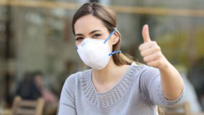 Woman doing thumbs up gesture wearing a protective mask avoiding contagion on a terrace