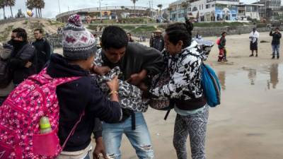 Un migrante centroamericano que lleva un niño recibe ayuda luego de ser rociado por agentes de la Patrulla Fronteriza de los EE. UU. Mientras intentaba cruzar la valla fronteriza.