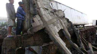 Habitantes observan los daños producidos por las copiosas lluvias que causaron el hundimiento de un terreno donde se ubica un predio de vehículos pesados y ello causó que un muro de concreto y un contenedor estacionado en el lugar cayera sobre unas viviendas en Villa Nueva (Guatemala).Foto EFE/Esteban Biba