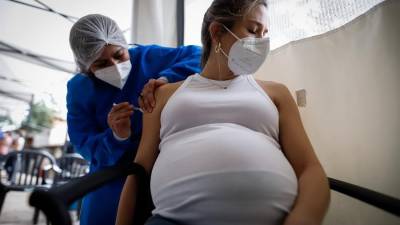 Personal médico aplicando una dosis de la vacuna Moderna a una mujer embarazada.