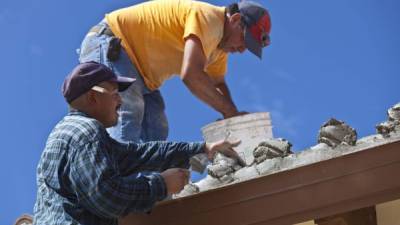 Dos maestros de obra de origen latino trabajan en la edificación de una vivienda.