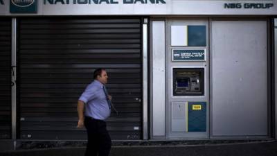 Un transeúnte camina frente a un cajero automático en las calles de Atenas. Foto: AFP