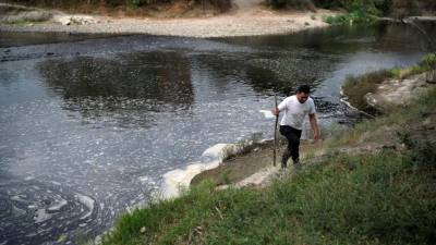Un hombre camina a orillas del contaminado río Lempa en Pinuelas, a 430 kilómetros al oeste de Tegucigalpa, Honduras, el 11 de enero de 2019. - El cambio climático y la contaminación generada por las aguas residuales de los municipios cercanos y los residuos del procesamiento industrial del café, son los principales factores de la hambruna en la cuenca del río Lempa en Guatemala, Honduras y El Salvador.