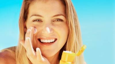 Portrait of attractive young female applying sunscreen to face