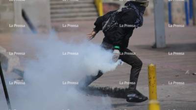 Un joven toma una bomba lacrimógena para devolverla a la Policía.