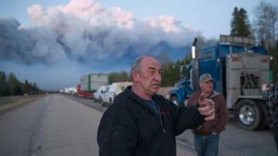 Una larga fila de camiones lleva suministros para combatir los incendios. Un espeso muro de humo se aprecia al fondo.
