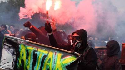 Protestors dressed in black and with the face covered, hold smoke bombs and a banner reading 'Attak' as they take part in a march for the annual May Day workers' rally, in Paris, on May 1, 2018. / AFP PHOTO / Alain JOCARD
